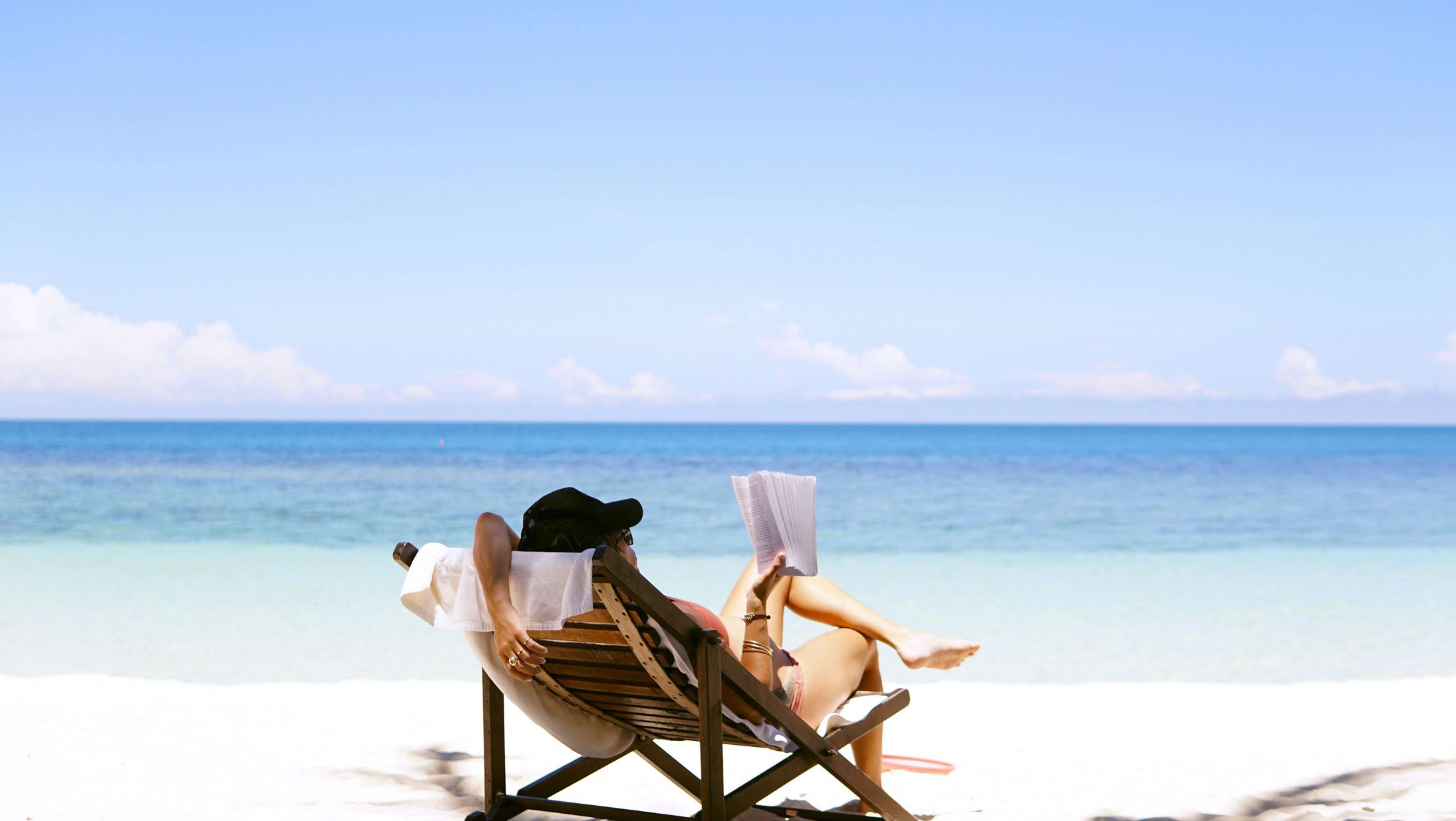 A woman reading in a beach chair by a calm turquoise sea